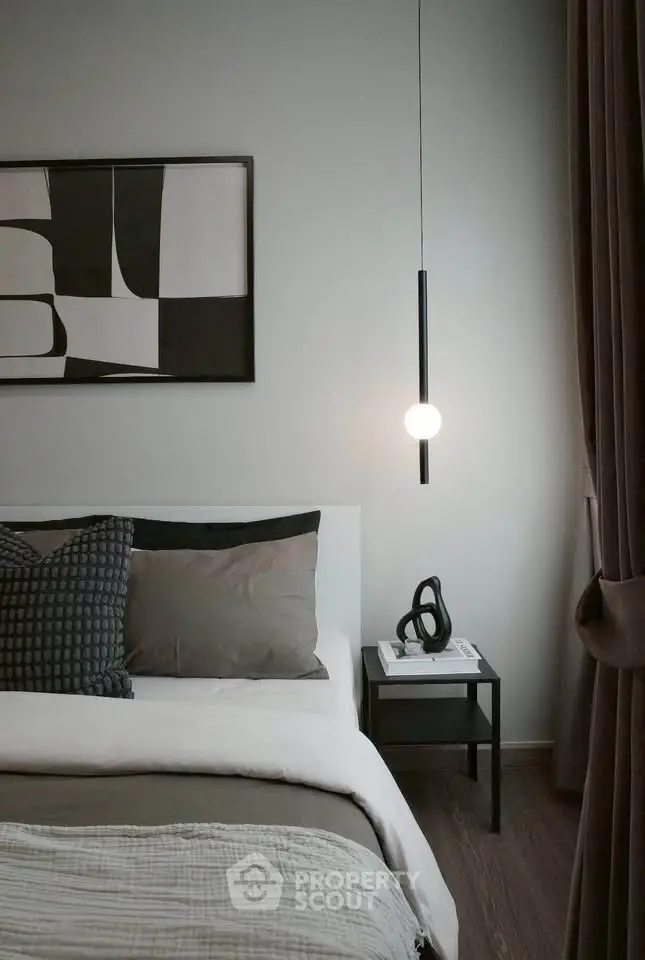 Modern bedroom with stylish decor and cozy ambiance, featuring a sleek pendant light and abstract wall art.