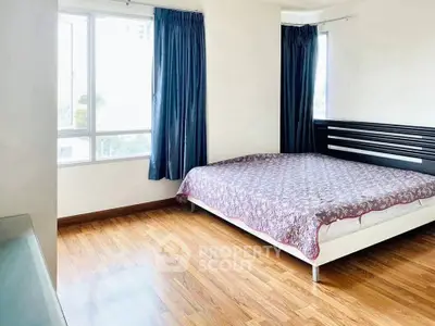 Spacious bedroom with wooden flooring and large windows for natural light