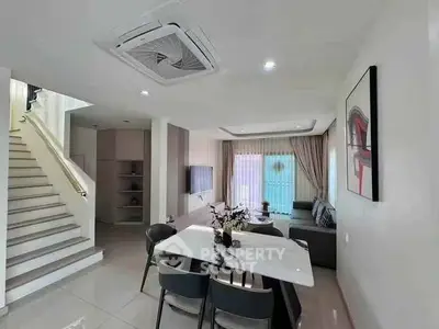 Modern living room with dining area and staircase, featuring sleek furniture and contemporary decor.