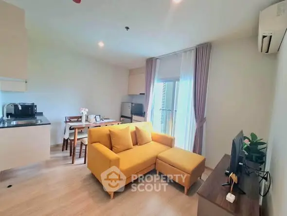 Modern living room with vibrant yellow sofa and open kitchen layout in a cozy apartment.