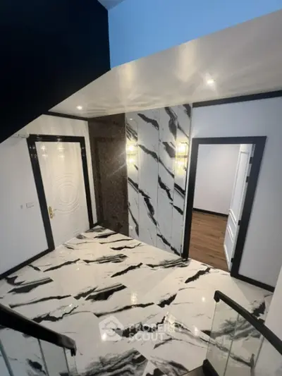 Luxurious marble-floored entryway with elegant wall patterns, modern lighting, and sophisticated design leading to multiple doors.