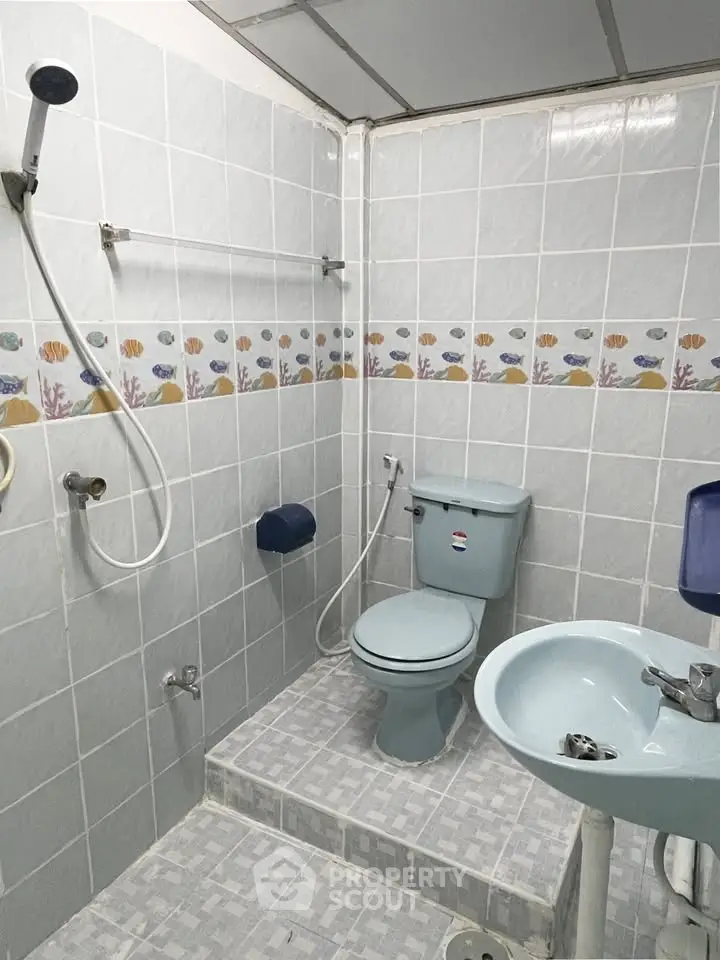 Compact bathroom with shower, toilet, and sink, featuring aquatic-themed tile border.