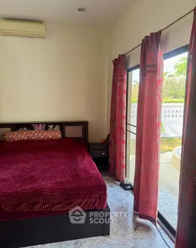 Cozy bedroom with large window and garden view, featuring elegant red bedding and stylish curtains.