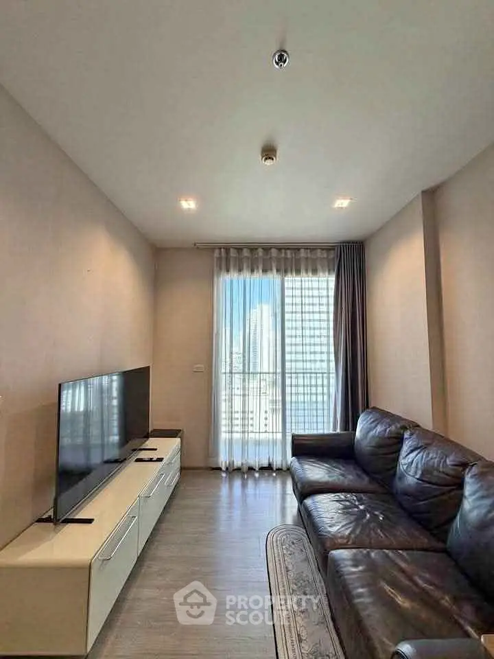 Modern living room with leather sofa and large TV, featuring floor-to-ceiling windows with city view.