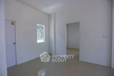 Spacious minimalist room with white walls and tiled floor, featuring natural light from a window.