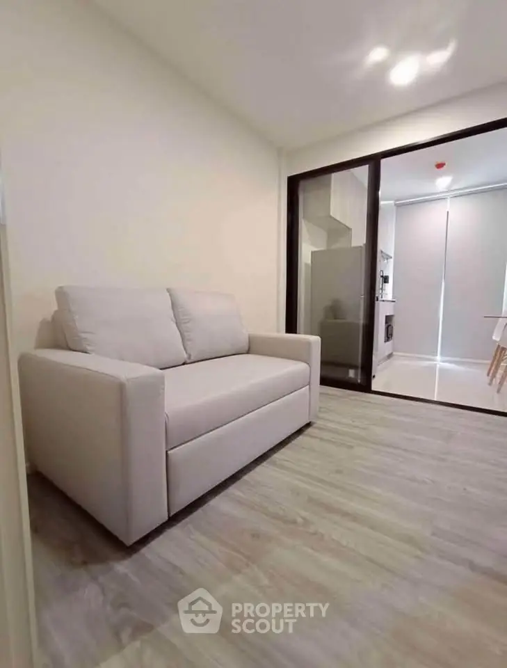 Modern living room with cozy sofa and sliding glass doors leading to kitchen area.