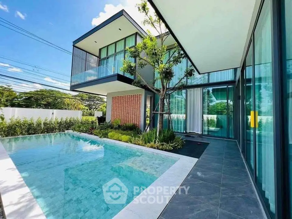 Modern luxury home with sleek architecture and private pool, surrounded by lush greenery and large glass windows.