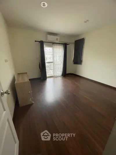 Spacious empty room with wooden flooring and large window for natural light.