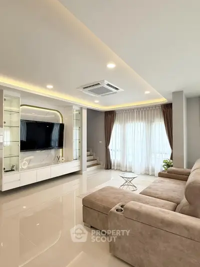 Spacious modern living room with plush sofa and large TV, featuring elegant lighting and floor-to-ceiling windows.