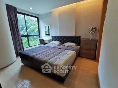 Spacious bedroom with large window and modern decor, offering a serene view of greenery.