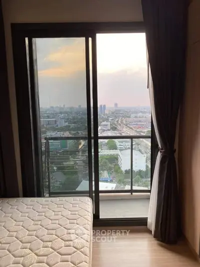 Cozy bedroom with balcony offering stunning city view at sunset.
