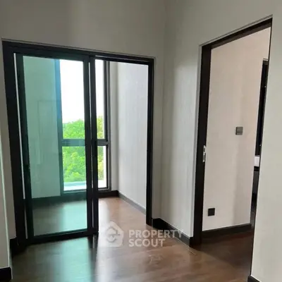 Modern apartment interior with glass doors leading to a balcony, featuring sleek wooden flooring.