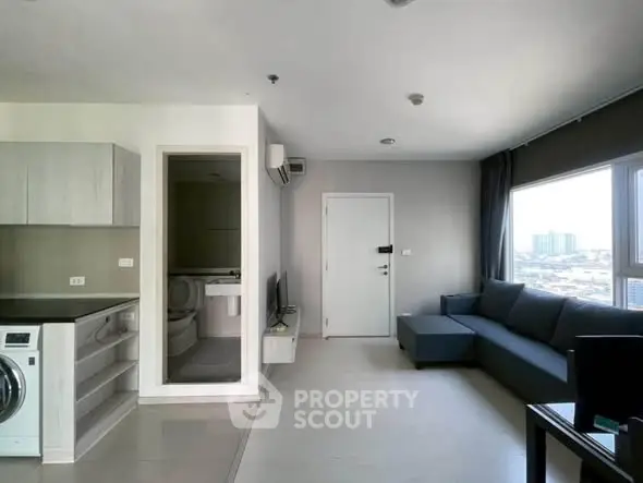 Modern living room with sleek furniture and city view, featuring a washing machine and open layout.