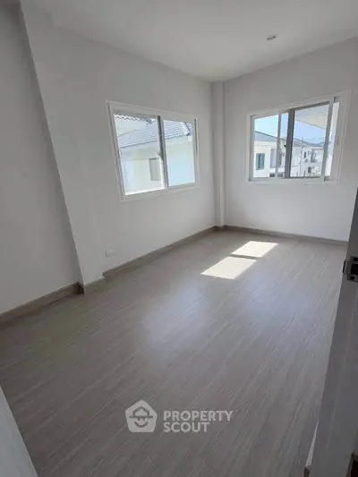 Bright empty room with large windows and modern flooring in a new residential property.