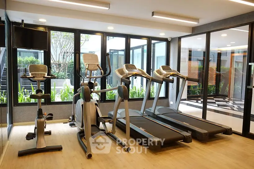 Modern gym with state-of-the-art equipment and large windows in luxury apartment complex.