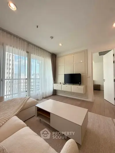 Modern living room with natural light, cozy seating, and sleek TV setup in a stylish apartment.