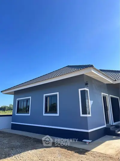 Modern single-story house with blue exterior and tiled roof under clear blue sky.