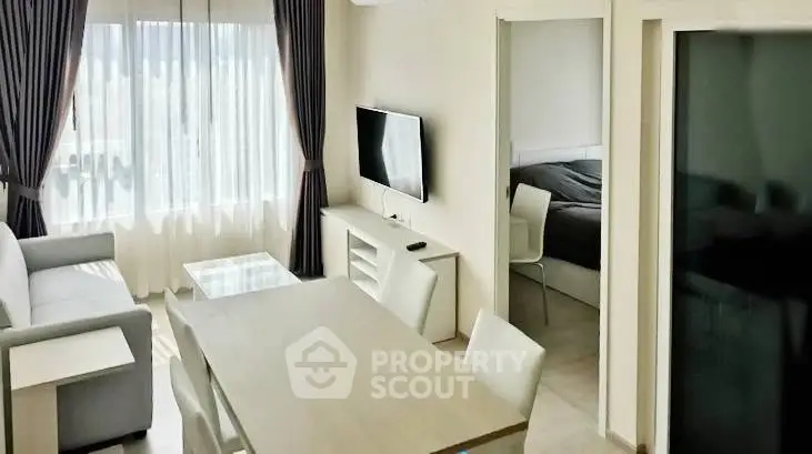 Modern living room with dining area and bedroom view, featuring sleek furniture and natural light.