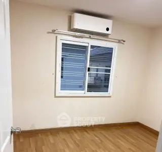 Spacious empty room with wooden flooring and air conditioning unit.