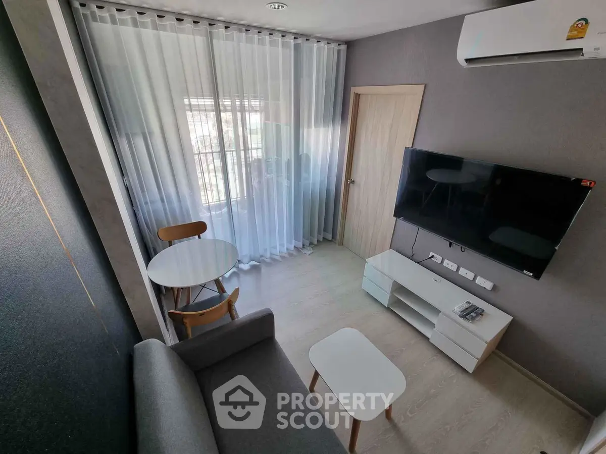 Modern living room with sleek furniture and wall-mounted TV, featuring a cozy seating area and natural light.