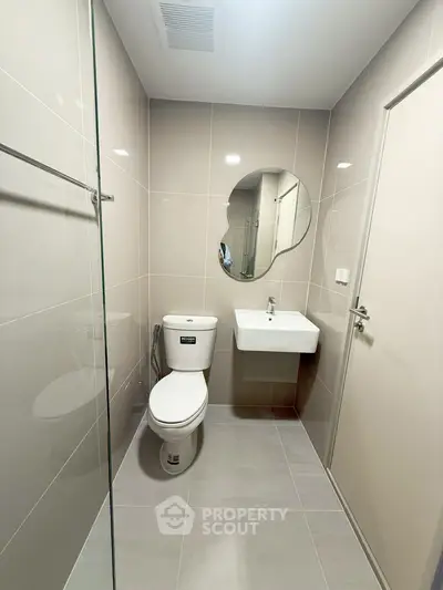 Modern bathroom with sleek design and round mirror, featuring neutral tiles and contemporary fixtures.