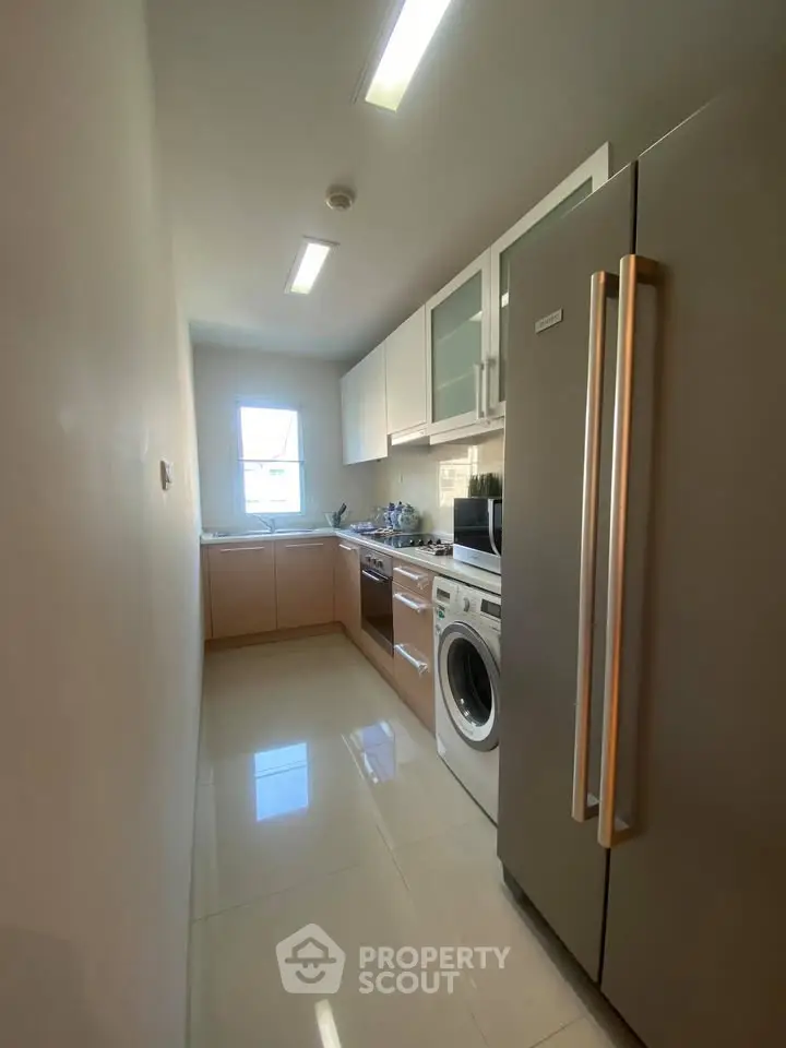 Modern kitchen with sleek appliances and ample natural light, featuring a washing machine and large fridge.