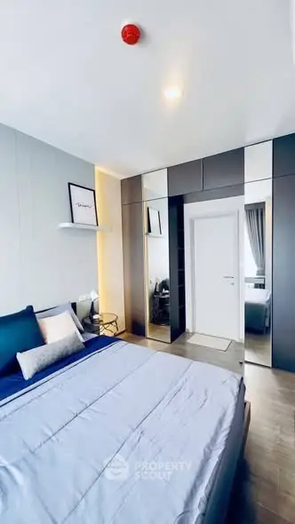 Modern bedroom with sleek design and ample natural light, featuring a stylish bed and mirrored wardrobe.