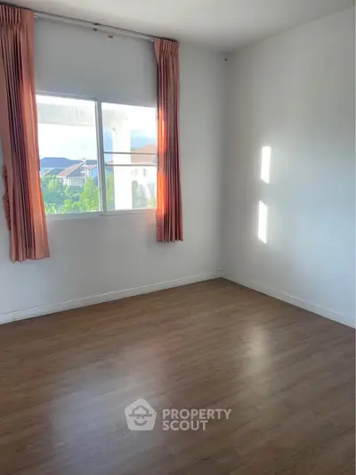 Bright empty room with wooden flooring and large window with pink curtains.