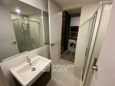 Modern bathroom with glass shower and washing machine in adjacent room.
