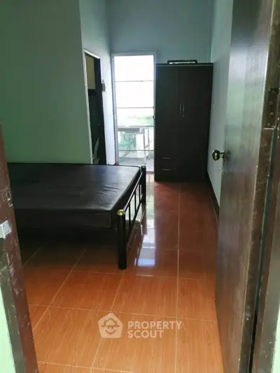 Cozy bedroom with wooden flooring and natural light through a window.