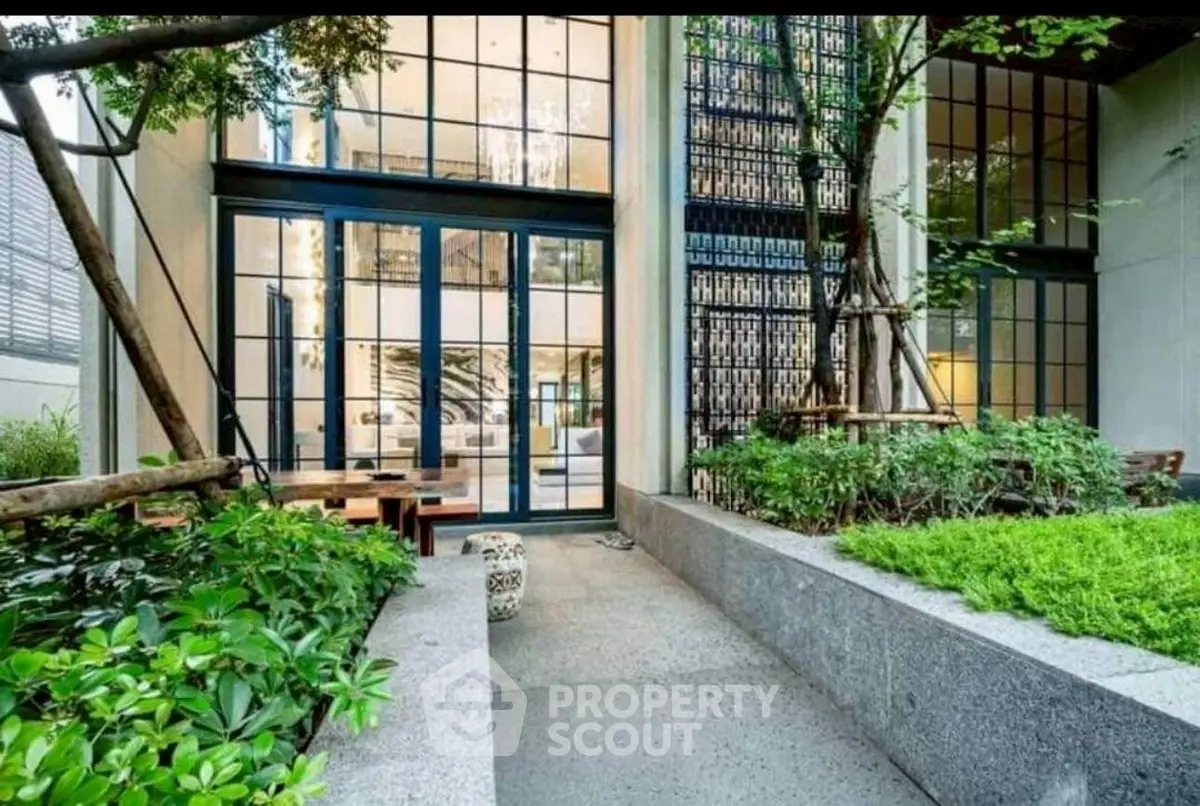 Modern building entrance with lush greenery and large glass windows, offering a welcoming ambiance.
