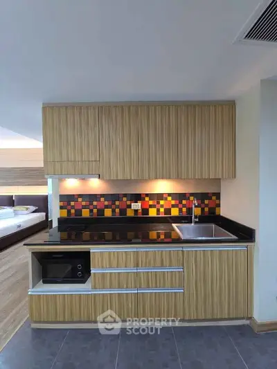 Modern kitchen with colorful backsplash and sleek cabinetry in open layout apartment.