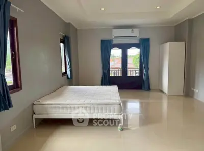 Spacious bedroom with large windows and balcony access, featuring minimalist decor and ample natural light.