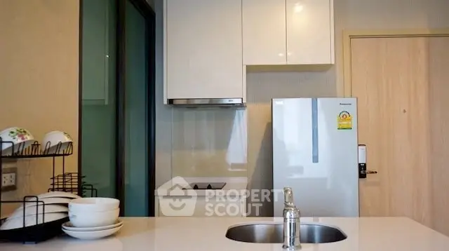 Modern kitchen with sleek cabinetry and stainless steel fridge in cozy apartment.