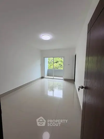 Spacious empty room with glossy tiled floor and large window leading to balcony.