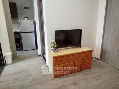 Cozy living area with TV and wooden dresser, adjacent to modern kitchen with fridge.