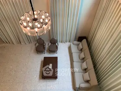 Elegant living room with high ceiling and modern chandelier, featuring plush seating and stylish decor.