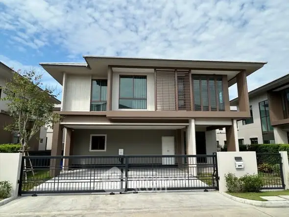 Modern two-story house with large windows and gated driveway under a clear blue sky.