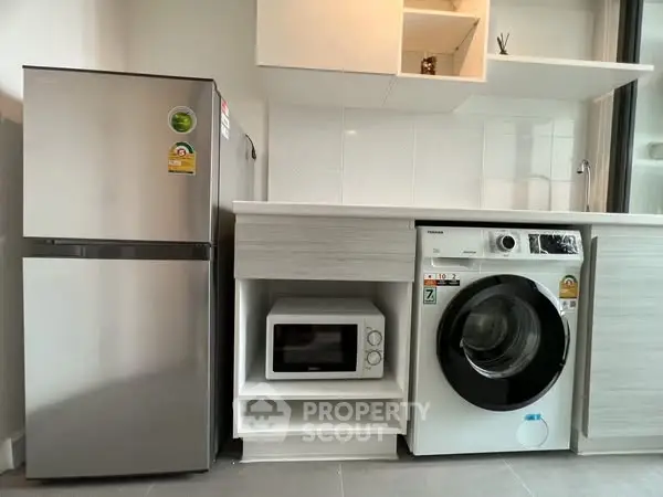 Modern kitchen with fridge, microwave, and washing machine in sleek design.