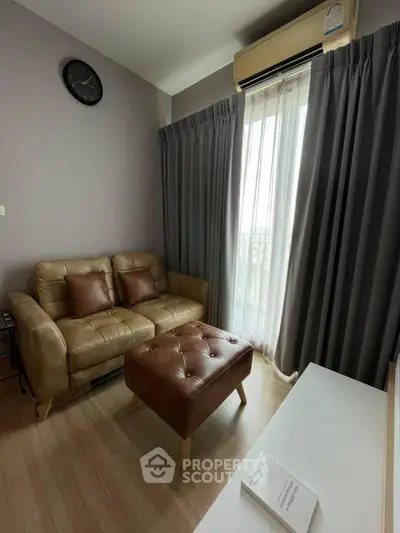Cozy living room with leather sofa, ottoman, and natural light from large window.