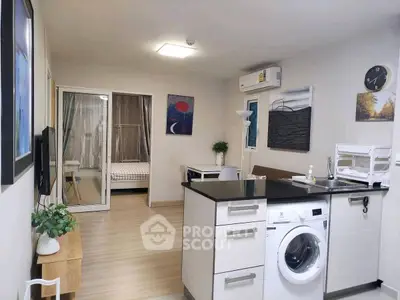 Modern open-plan living room with kitchen and washing machine, featuring stylish decor and natural light.