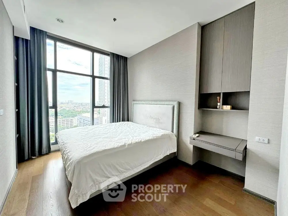 Modern bedroom with large window and city view, featuring sleek built-in desk and cozy ambiance.