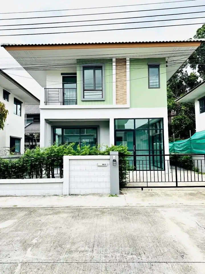 Modern two-story house with green facade and large windows in a suburban neighborhood.