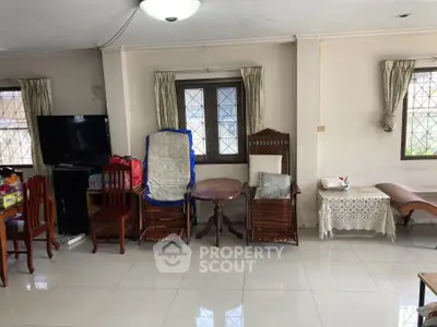 Spacious living room with tiled floors, wooden furniture, and natural light from large windows.