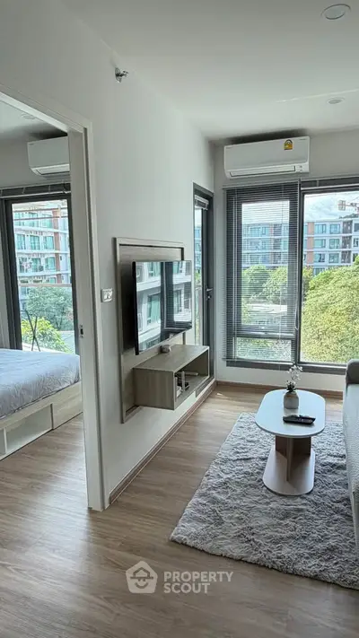 Modern apartment living room with TV, cozy rug, and view of cityscape through large windows.