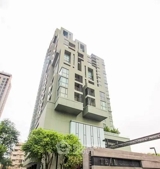 Modern high-rise building with unique architectural design and lush greenery at the base.