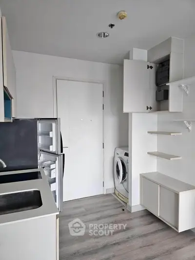 Modern kitchen with sleek cabinetry, washing machine, and compact fridge in a minimalist design.