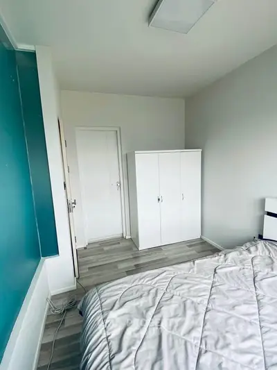 Modern bedroom with minimalist design and white furniture, featuring a cozy bed and sleek wardrobe.
