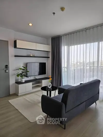 Modern living room with sleek furniture and large window offering natural light.