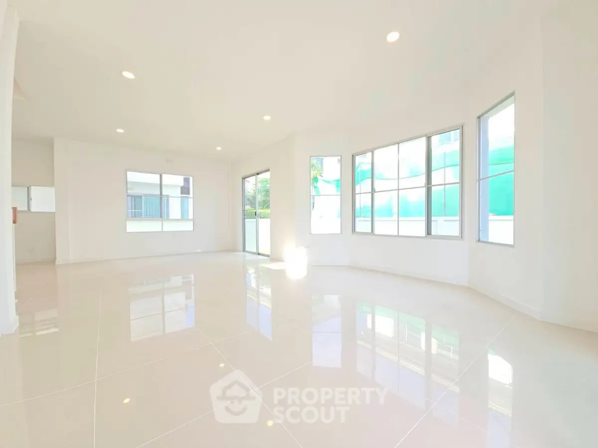 Spacious sunlit living room with large windows and glossy tiled floors